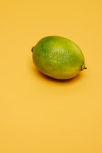 Close-up of a single fresh green lime on a vibrant yellow background.